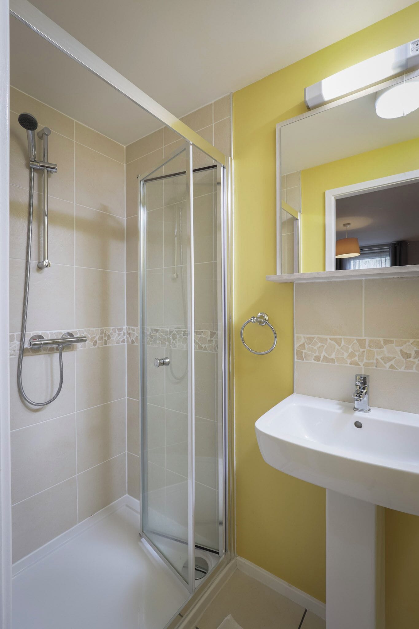 Une salle de bain avec une douche à l’italienne, un lavabo blanc et un mur jaune.