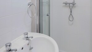 A modern bathroom with a glass shower enclosure, a white sink with two faucets, and a mirror above the sink. - Devon Guest House (Blackpool)