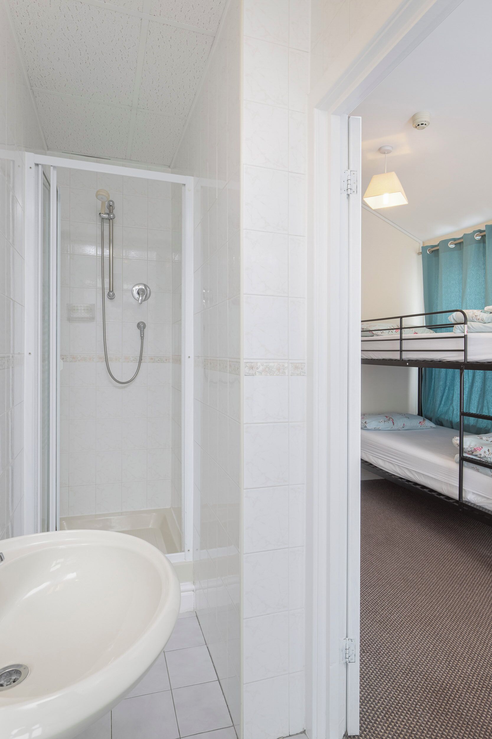 A bathroom with a shower, a sink, and a bunk bed in the adjacent room.