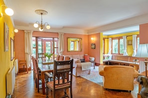 A spacious living room with a dining area, wooden flooring, and large windows.