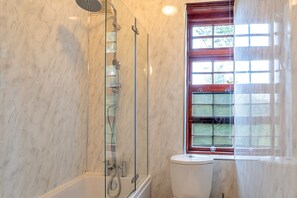 A bathroom with a glass-enclosed shower, a toilet, and a window with a view of greenery.
