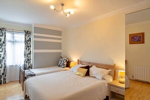 A bedroom with two beds, a window with curtains, a radiator, and a painting on the wall.