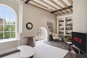 A spacious living room with a large window, a fireplace, a bookshelf, and a television. - Preacher's Yard Stylish Central York Apartment - Duplex 3 (York)