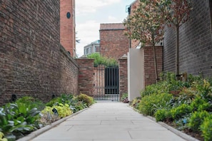 A narrow alleyway with brick walls, a gated entrance, and a pathway lined with greenery. - Preacher's Yard Stylish Central York Apartment - Duplex 3 (York)