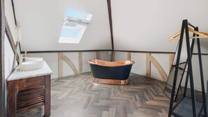 Un baño estilo loft con una bañera independiente, un tocador de madera y un tragaluz.