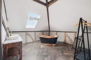 Ein Loft-Badezimmer mit freistehender Badewanne, einem Holzwaschtisch und einem Oberlicht.