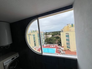Une pièce dotée d’une grande fenêtre donnant sur une piscine et les bâtiments adjacents.