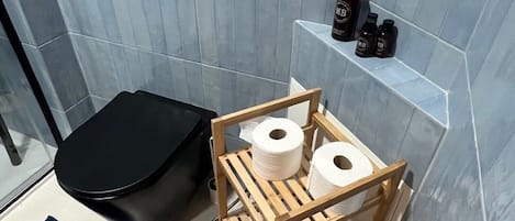 A bathroom with a toilet, a wooden shelf with toiletries, and a shower area.