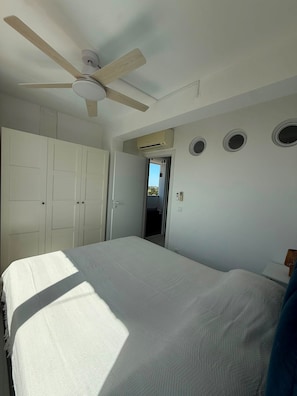 Une chambre à coucher comprenant un lit, un ventilateur de plafond, une armoire et une porte donnant sur une autre pièce.