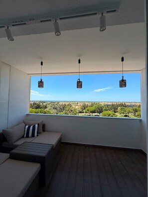 A balcony with a sofa and a table, overlooking a landscape with buildings and trees. - Reformed Vintage Top Floor Stunning Views by Bento Box (Quarteira)