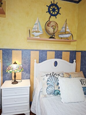 Une chambre à coucher avec un lit, une table de chevet avec une lampe, un globe terrestre et des décorations représentant des voiliers sur le mur.