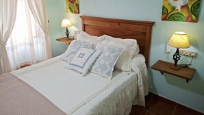 Un lit bien fait, avec une couverture à motifs et des oreillers, deux lampes de chevet, une tête de lit en bois et un mur orné de tableaux floraux.