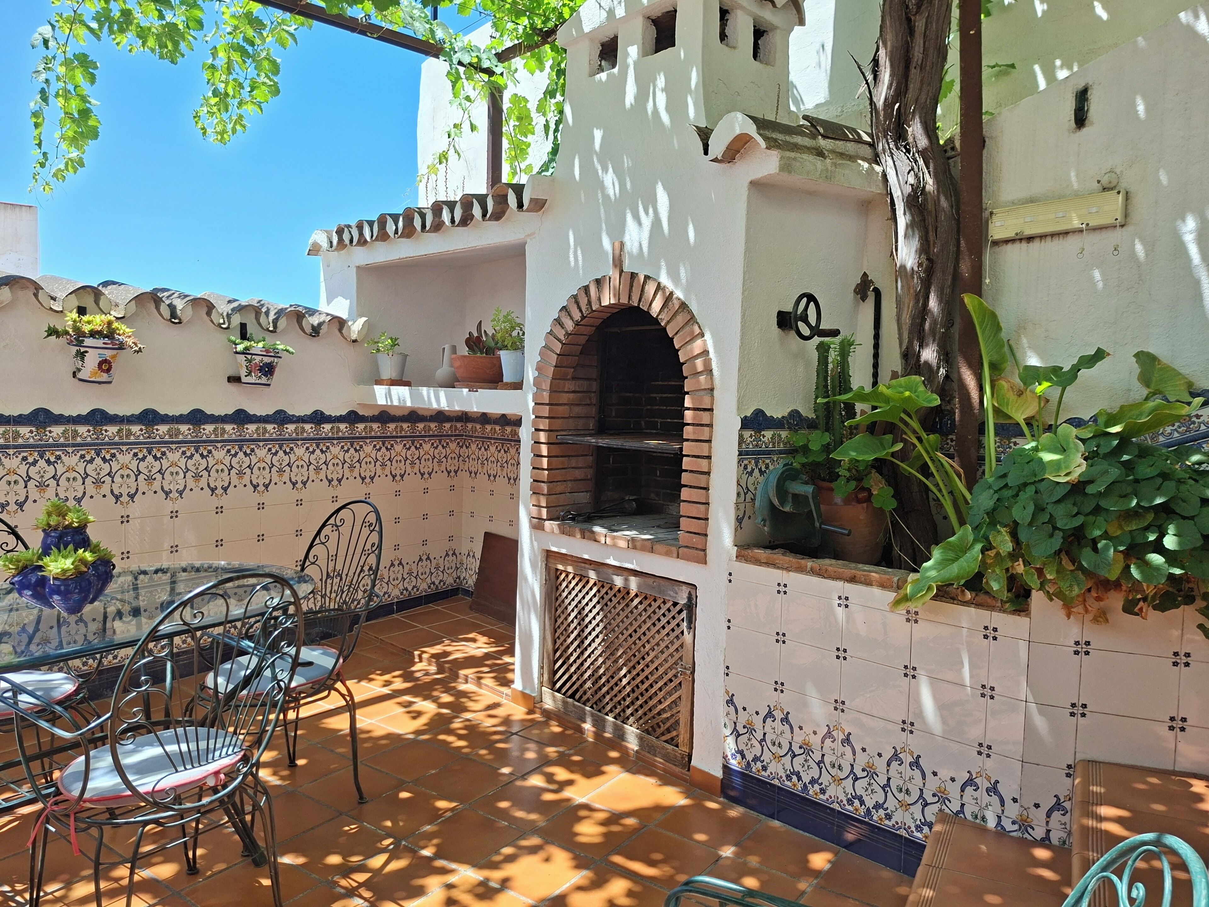 Un patio al aire libre con horno de ladrillo, paredes de azulejos, plantas en macetas y sillas de metal.