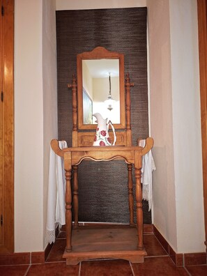 Une cheminée en bois surmontée d’un miroir, un pichet blanc et un luminaire suspendu.