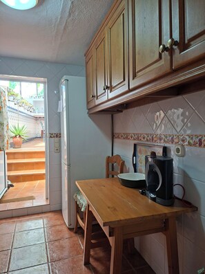 A kitchen with wooden cabinets, a refrigerator, a coffee maker, and a window with a view of the outside. - Casa Luciíta: Cozy, with a fireplace, patio, and BBQ. Near Marbella (Ojén)