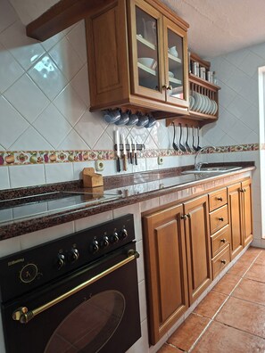 A kitchen with a stove, oven, wooden cabinets, and a tiled backsplash. - Casa Luciíta: Cozy, with a fireplace, patio, and BBQ. Near Marbella (Ojén)