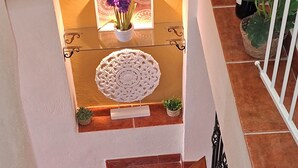 Un escalier en bois avec une rampe blanche, menant à un palier agrémenté d’un mur blanc décoratif et d’une petite plante en pot.