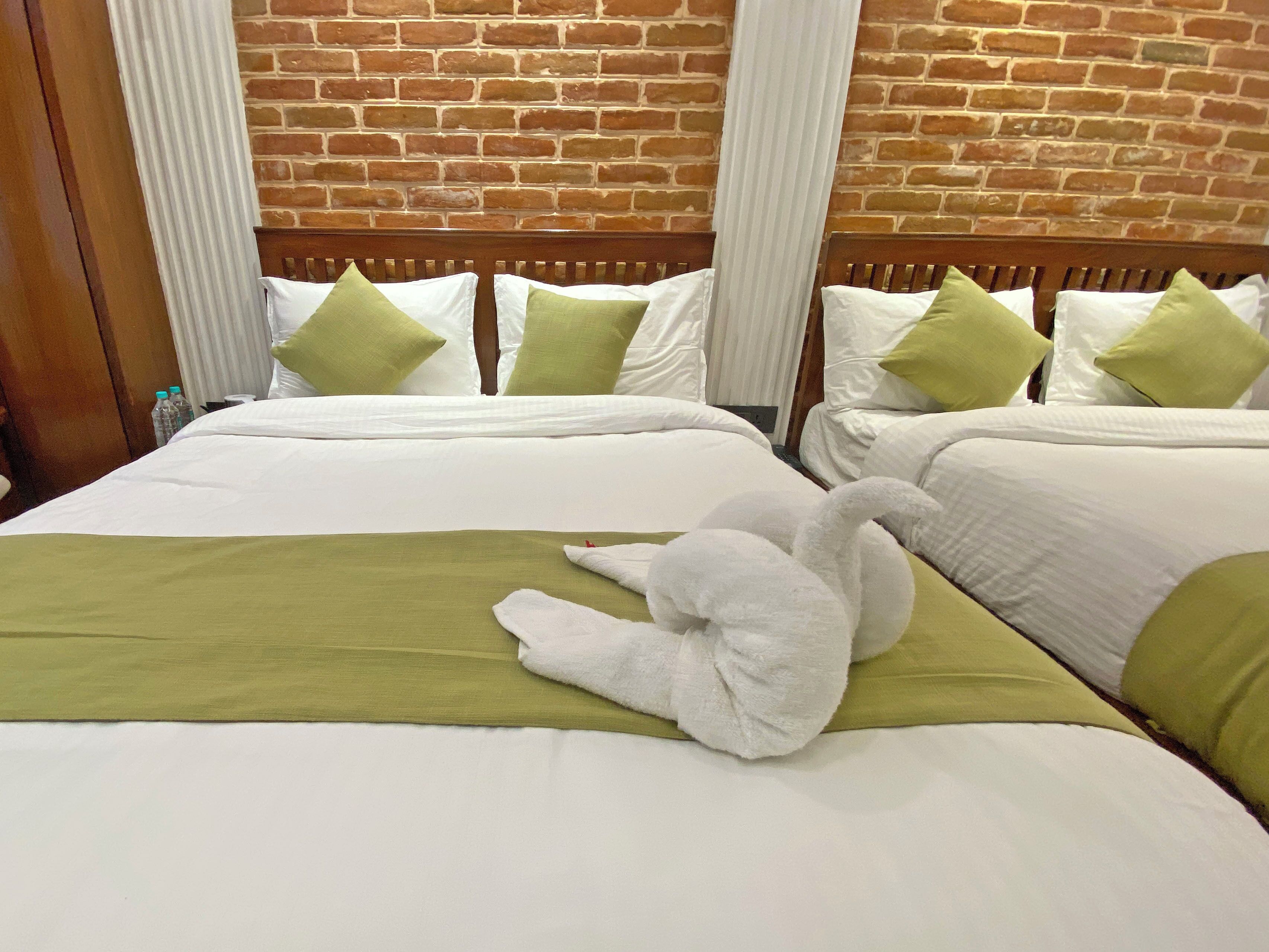 Habitación de hotel con dos camas, cada una con ropa de cama blanca y almohadas verdes. Una cama tiene una manta verde.
