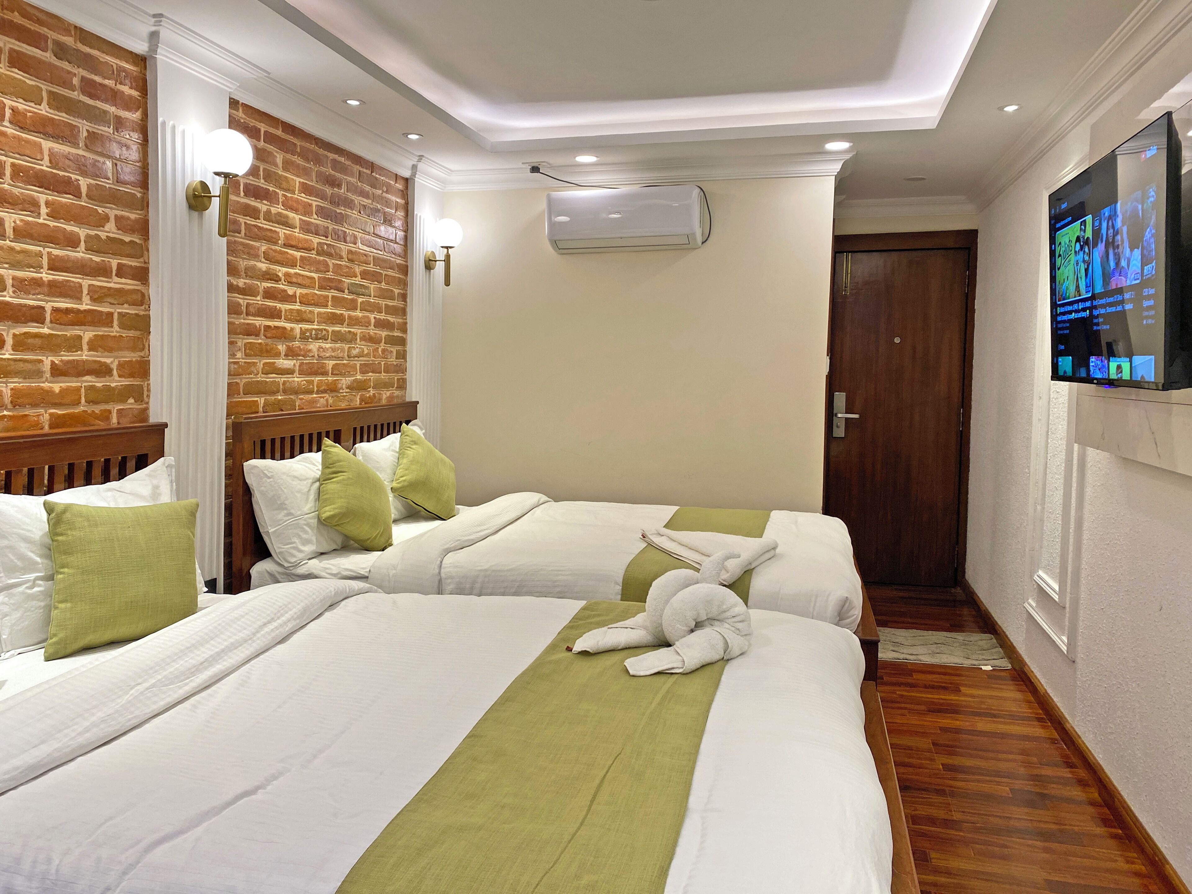 Una habitación de hotel con dos camas, una pared de ladrillo, un equipo de aire acondicionado y una televisión en la pared.