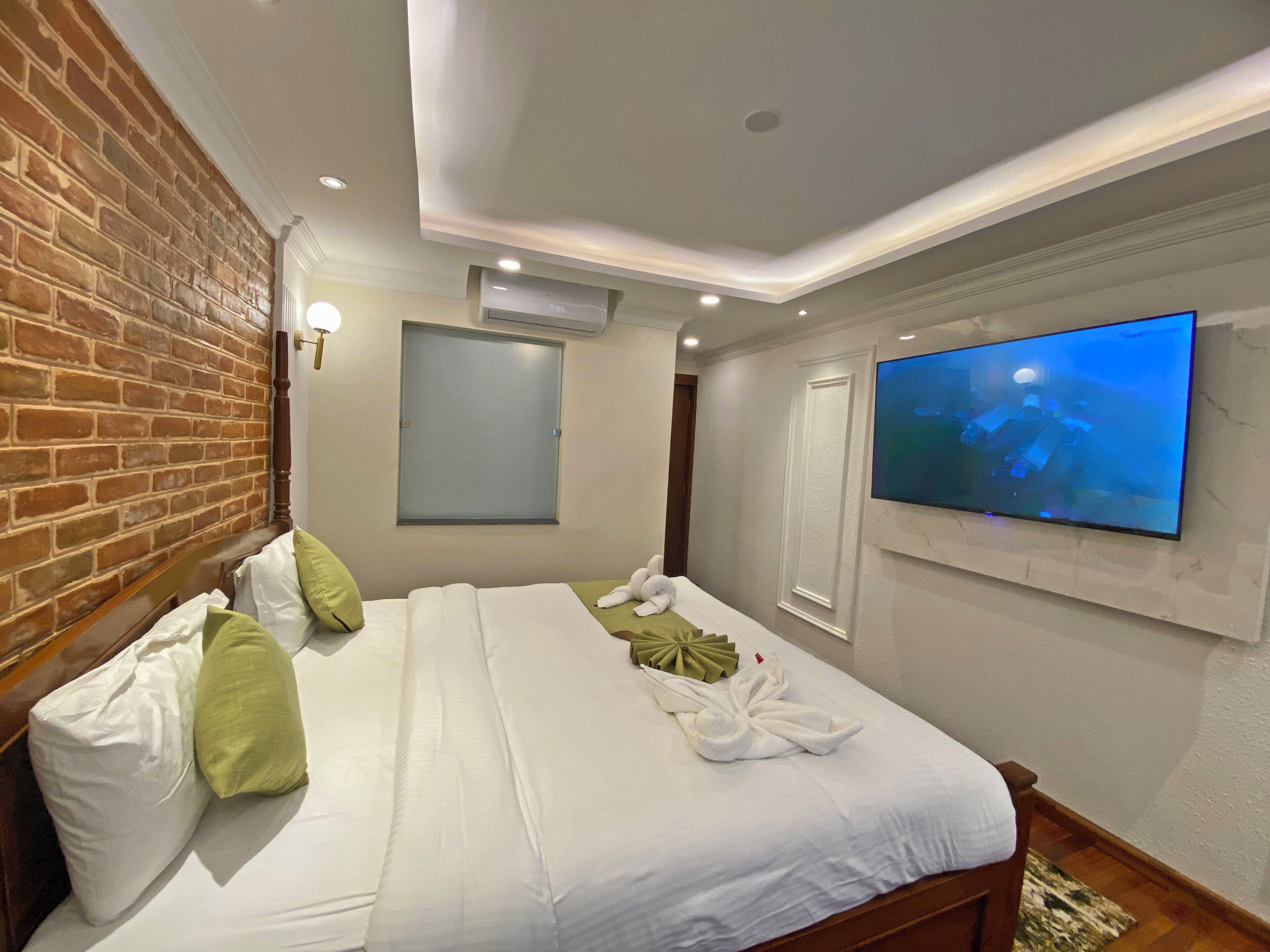 Habitación de hotel con pared de ladrillo, cama con ropa blanca, televisor de pantalla plana montado en la pared y ventana con vistas.