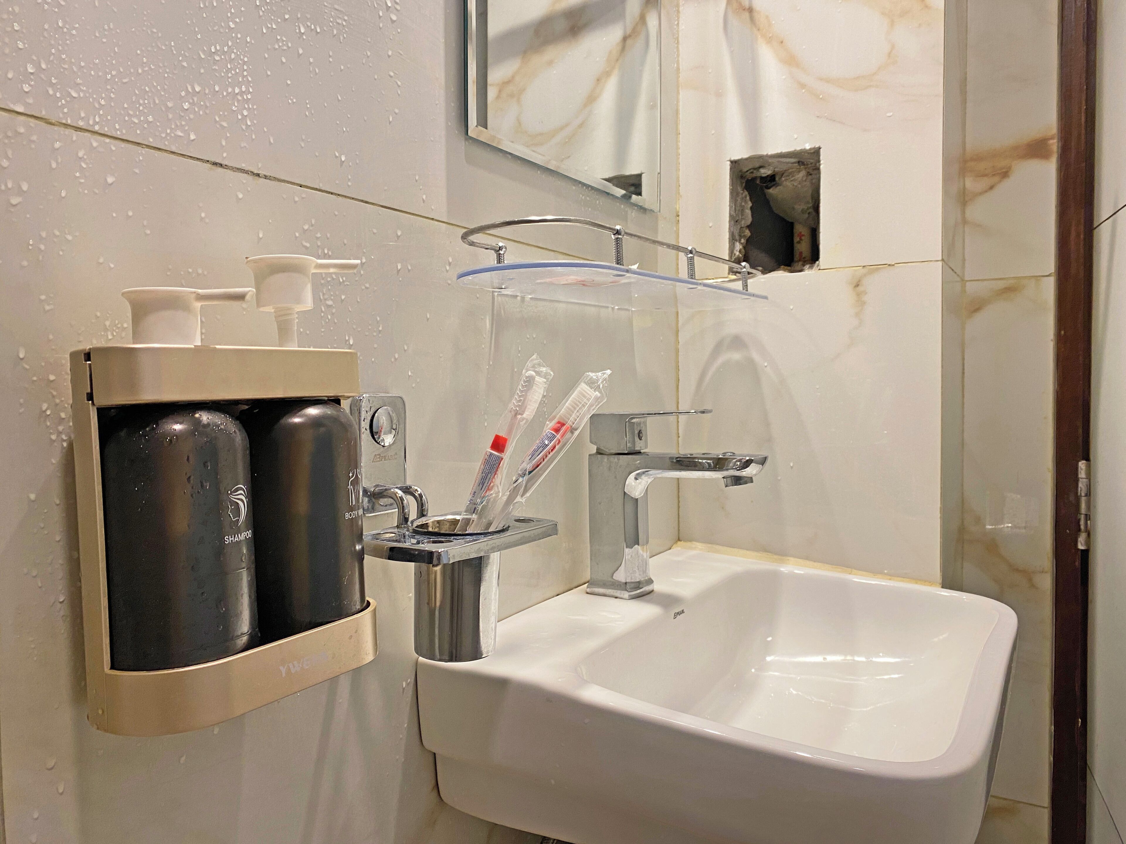 Un baño con un lavamanos blanco, un espejo y un estante con artículos de aseo, incluyendo champú y cepillos de dientes.
