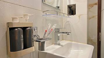 Un baño con un lavamanos blanco, un espejo y un estante con artículos de aseo, incluyendo champú y cepillos de dientes.