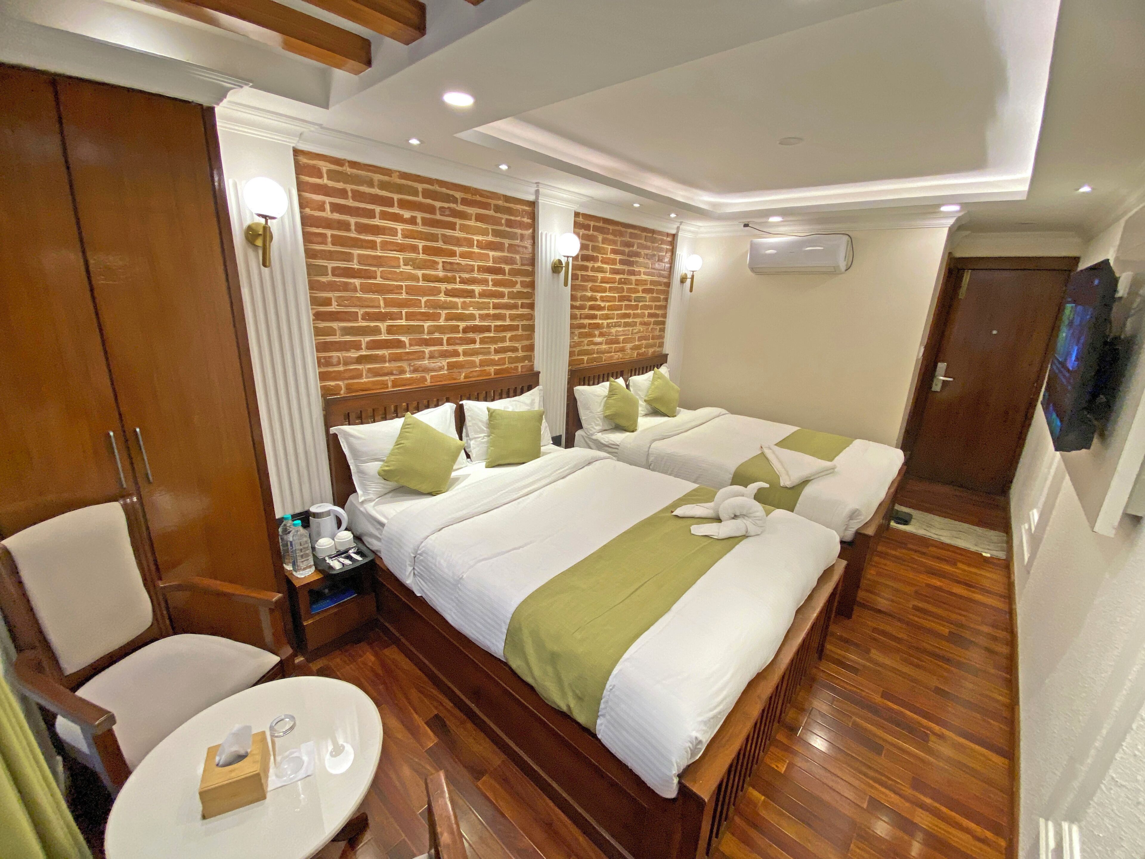 A hotel room with a brick wall, a wooden bed, a wooden wardrobe, a round table, and a television.