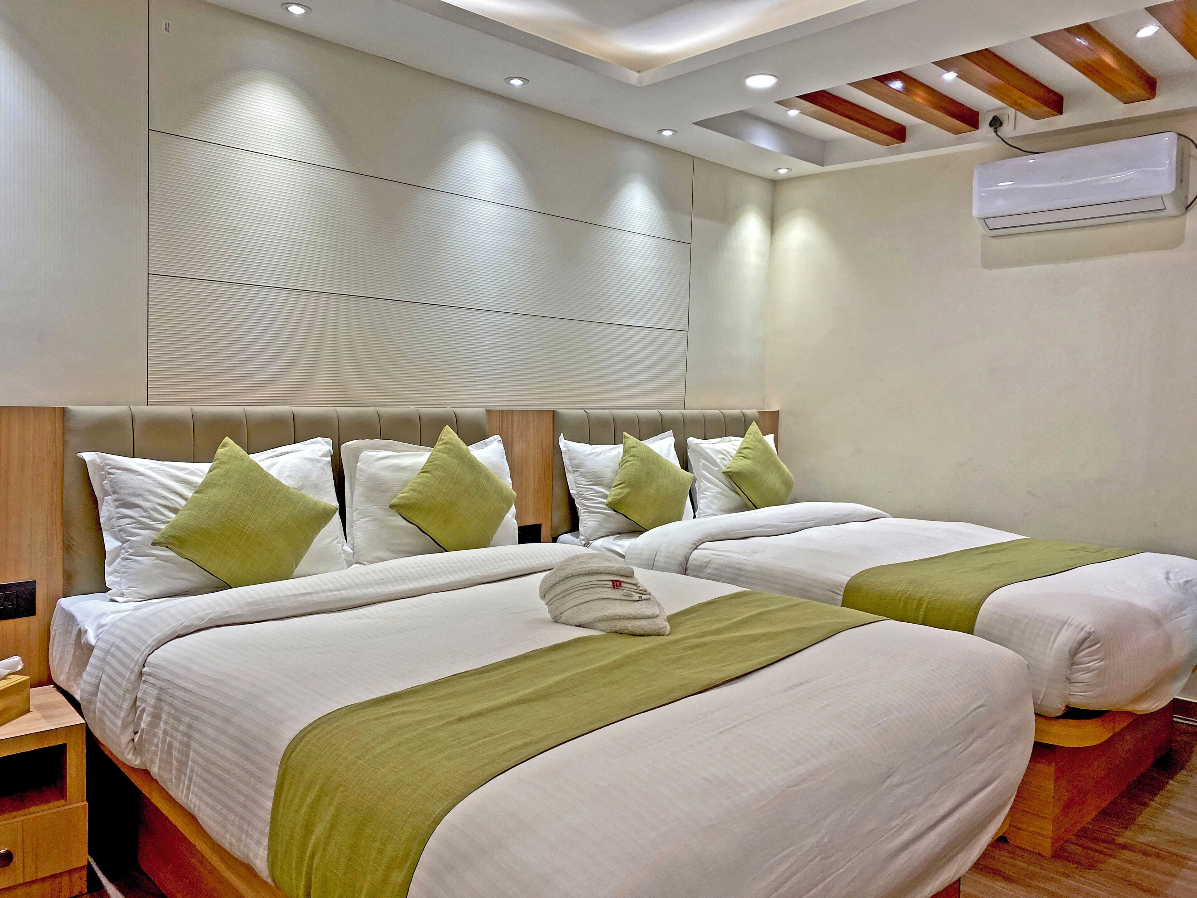 Habitación de hotel con dos camas, cabecero de madera, mesita de noche y un equipo de aire acondicionado en la pared.