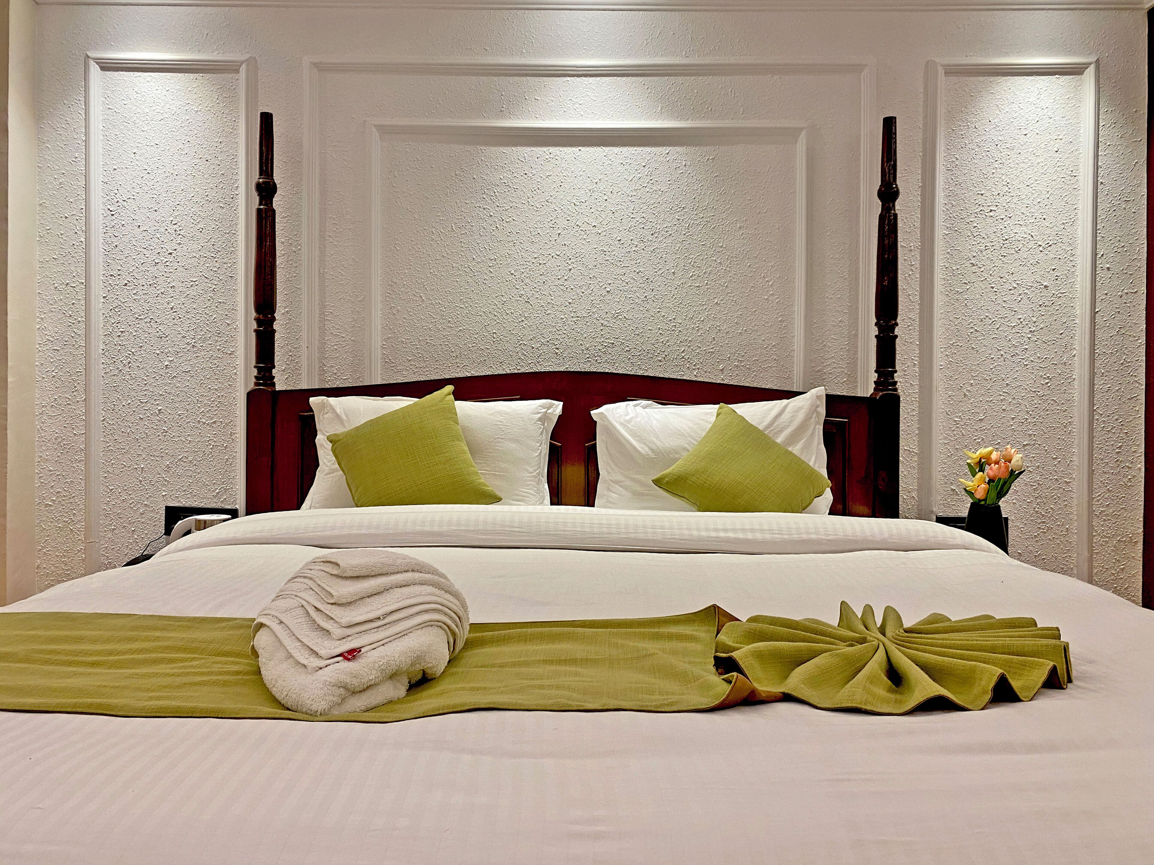A neatly made bed with pillows, a folded towel, and a green cloth on the bed.