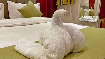 Una cama bien hecha con una almohada blanca, una almohada verde y un objeto blanco mullido que parece un cisne sobre un edredón verde.