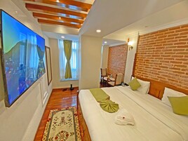 Habitación de hotel con un televisor de pantalla plana grande, cama con ropa de cama verde y blanca, pared de ladrillo decorativa y techo de madera.