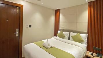Habitación de hotel con cama, una puerta de madera, una mesita de noche con teléfono y un panel de control en la pared.