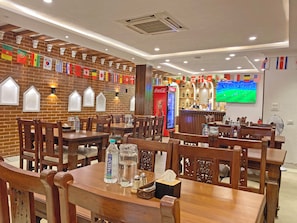 Un restaurante con paredes de ladrillo, mesas y sillas de madera. Hay banderas colgadas en la pared, y botellas y vasos sobre las mesas.