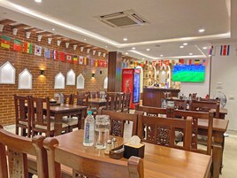 Un restaurante con paredes de ladrillo, mesas y sillas de madera. Hay banderas colgadas en la pared, y botellas y vasos sobre las mesas.