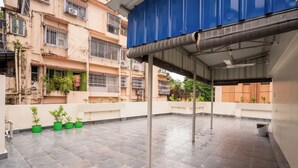 A rooftop terrace with tiled flooring, potted plants, and a blue awning. - Fithaus - A Boutique Stay (Kolkata)