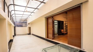 A spacious corridor with a glass table in the foreground, leading to a room with a wooden door and a chair. - Fithaus - A Boutique Stay (Kolkata)