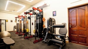 A gym with various exercise equipment, a door, and a wall-mounted air conditioner. - Fithaus - A Boutique Stay (Kolkata)