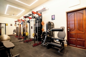 A gym with various exercise equipment, a door, and a wall-mounted air conditioner. - Fithaus - A Boutique Stay (Kolkata)