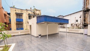 A rooftop terrace with a blue roof structure, a white wall, and a tiled floor. - Fithaus - A Boutique Stay (Kolkata)