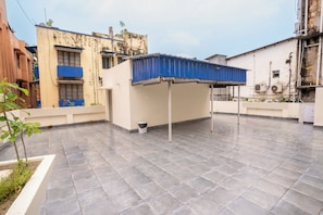 A rooftop terrace with a blue roof structure, a white wall, and a tiled floor. - Fithaus - A Boutique Stay (Kolkata)