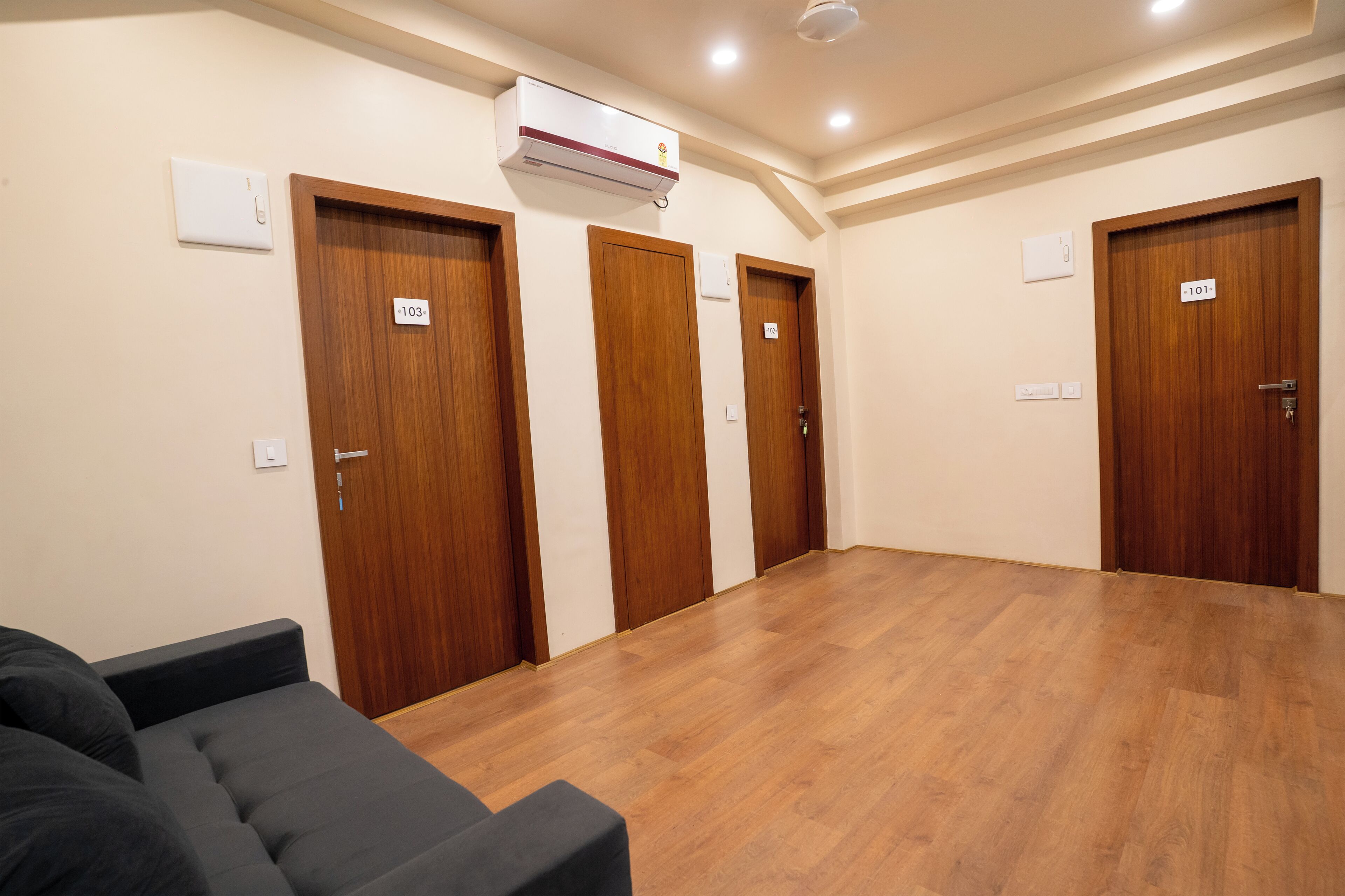 Habitación de hotel con puertas de madera, aire acondicionado instalado en el techo y un sofá de color oscuro.
