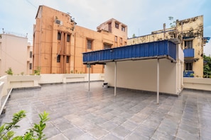 Une terrasse sur le toit, dotée d’une marquise bleue, d’un sol carrelé et offrant une vue sur les bâtiments adjacents.