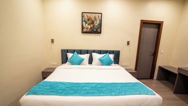 A hotel room with a large bed, two bedside tables, a door, and a painting on the wall. - Fithaus - A Boutique Stay (Kolkata)