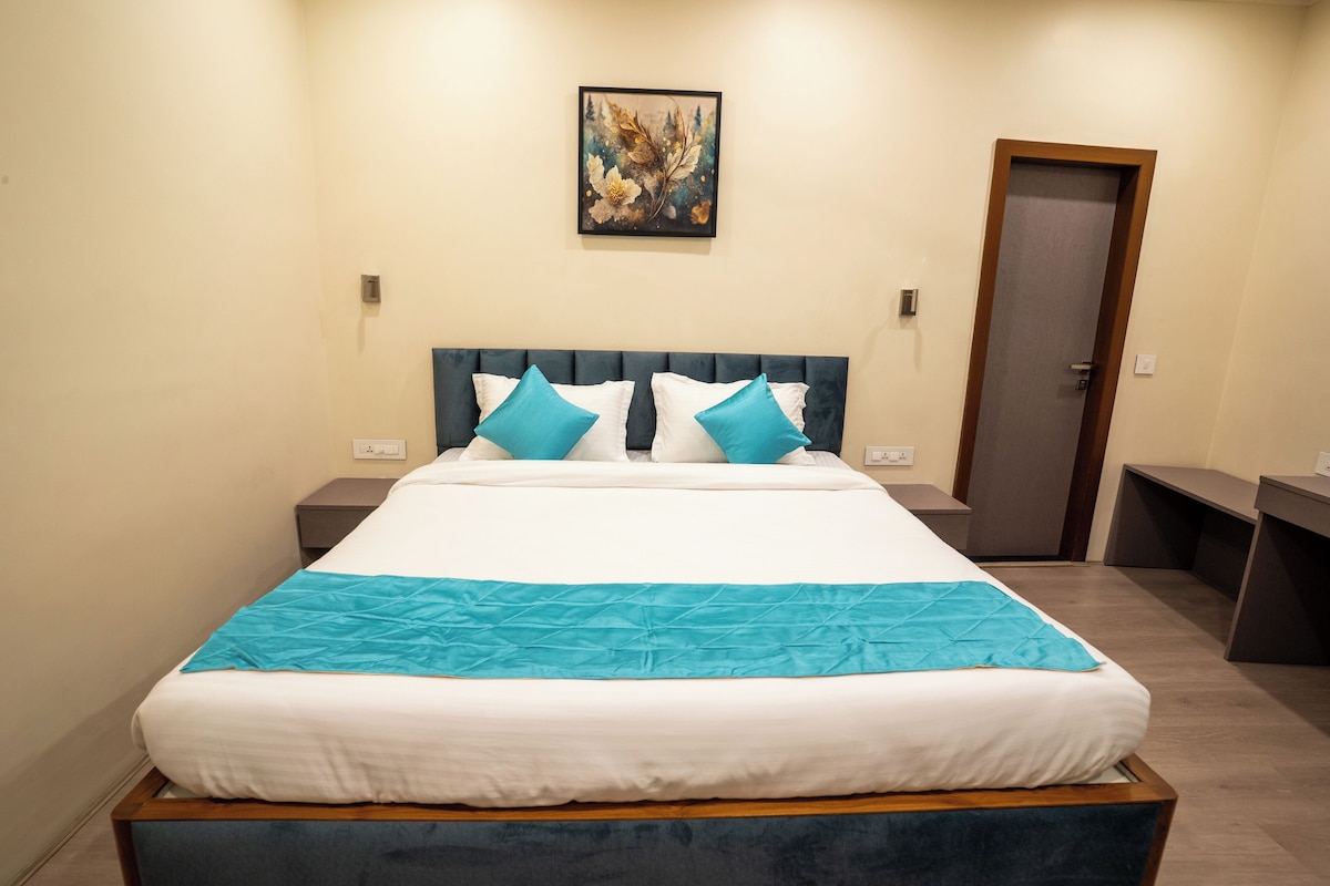 Una habitación de hotel con una cama grande, dos mesitas de noche, una puerta y un cuadro en la pared.