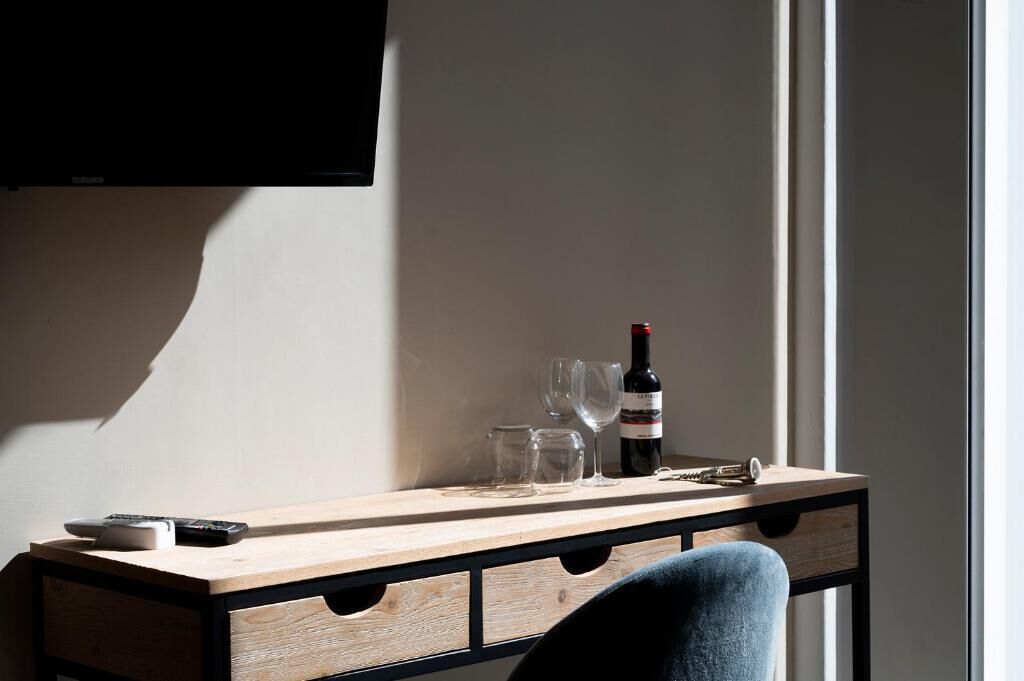 Un escritorio de madera con una botella de vino, copas y un control remoto.