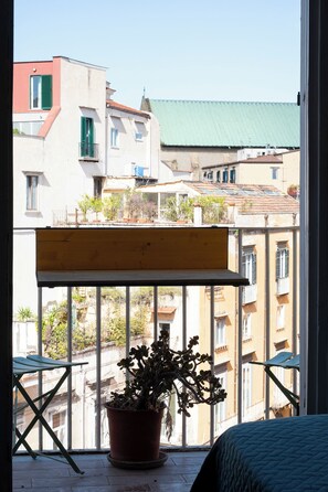 Ein Balkon mit einem Blumentopf, einer Holzbank und Blick auf Gebäude.