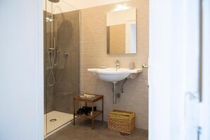 A modern bathroom with a glass-enclosed shower, a white sink, and a small wooden table. - Bellavista Relais (Napoli)