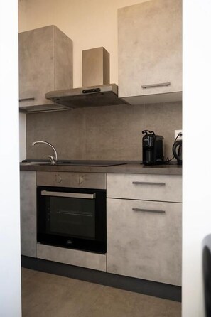 A kitchen with a built-in oven, a stainless steel range hood, and a coffee maker on the countertop. - Bellavista Relais (Napoli)