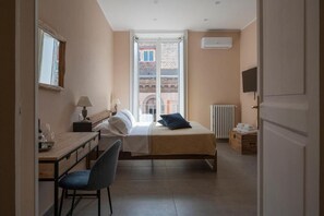 A hotel room with a bed, a desk, a chair, a window, and a radiator. - Bellavista Relais (Napoli)