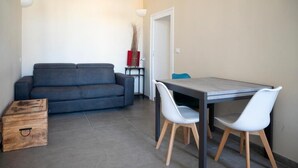 A modern living room with a grey sofa, a wooden chest, and a dining table with white chairs. - Bellavista Relais (Napoli)